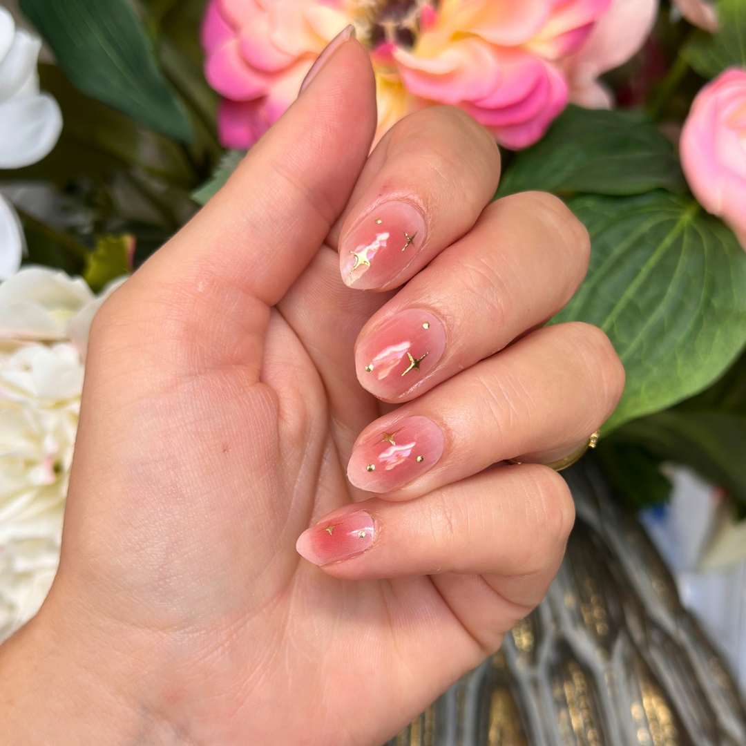 Roze gellakstickers met subtiel kleurverloop, gouden sterretjes en gouden details op amandelvormige nagels.