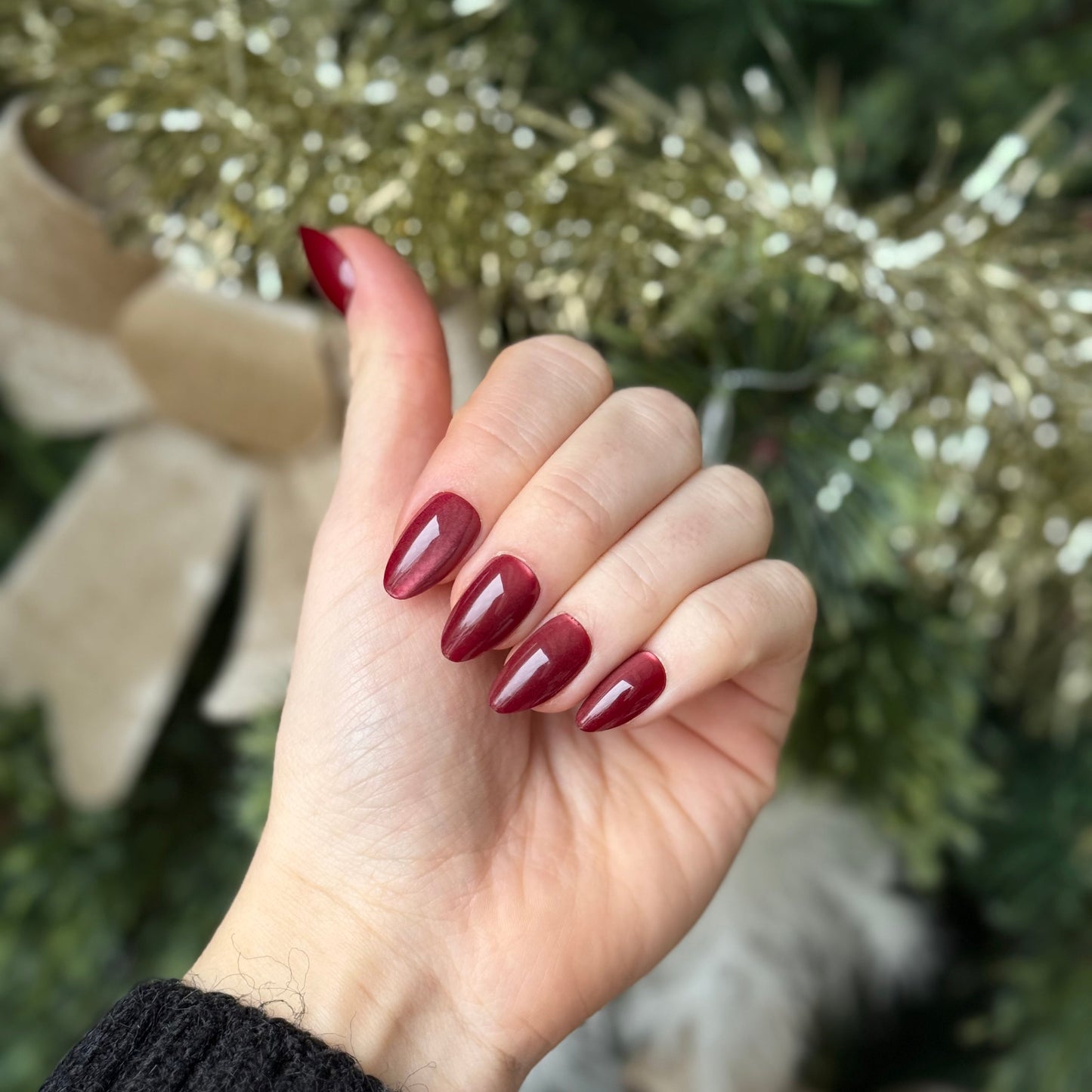 Rode almond vormige press-ons met een cat eye effect. Achtergrond is een kerstboom.